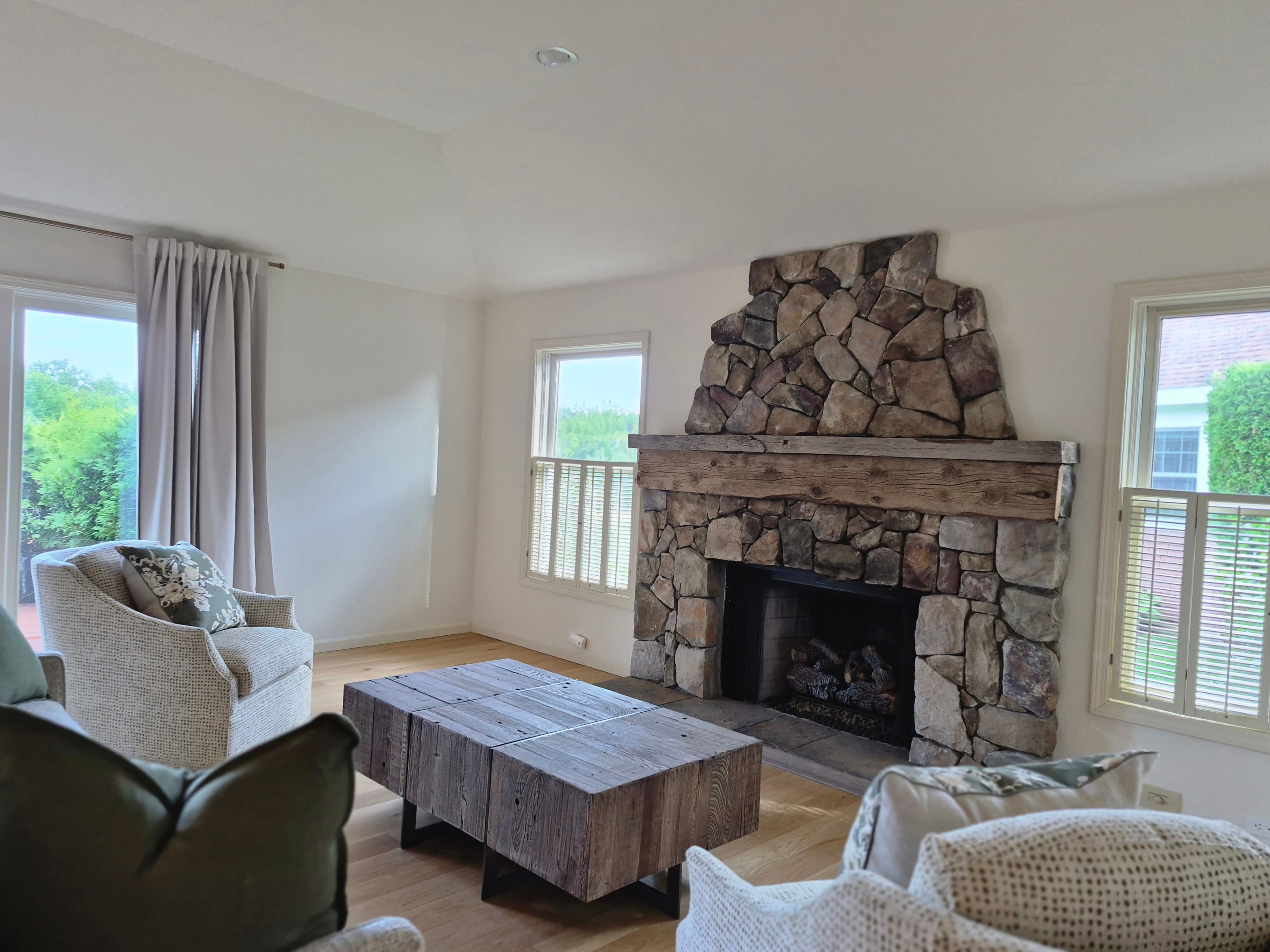 A bright living room with a stone fireplace and a wood coffee table, freshly cleaned